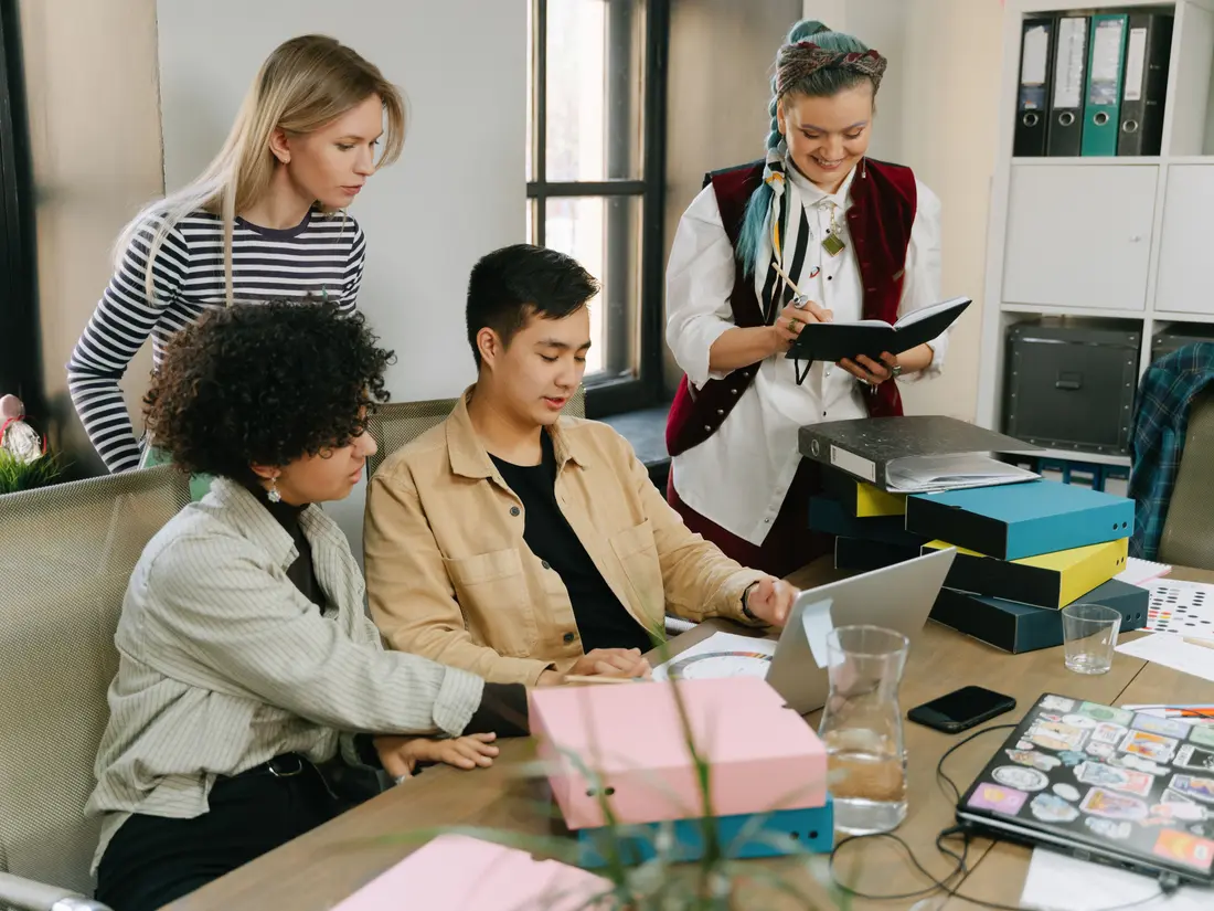 A group of colleagues gathered around a laptop in a shared workspace