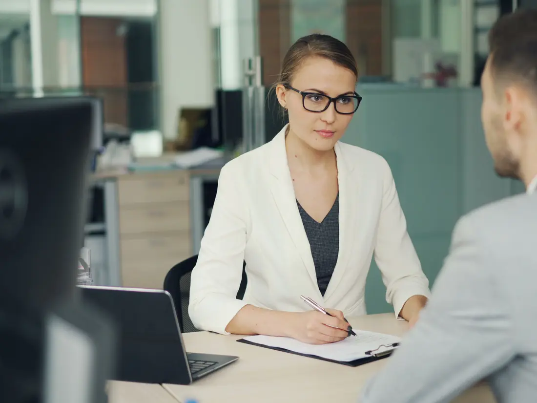 An HR interviewer taking notes across a desk from a candidate