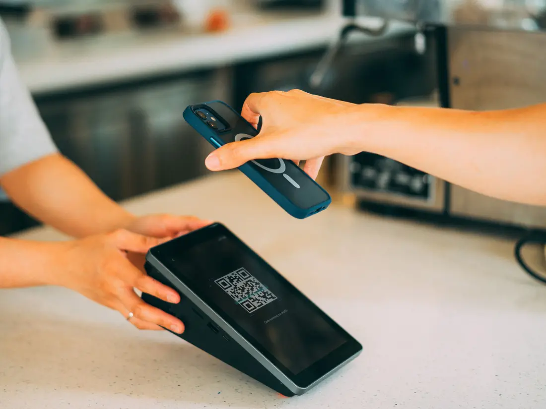 A customer holding a phone over a payment terminal displaying a QR code